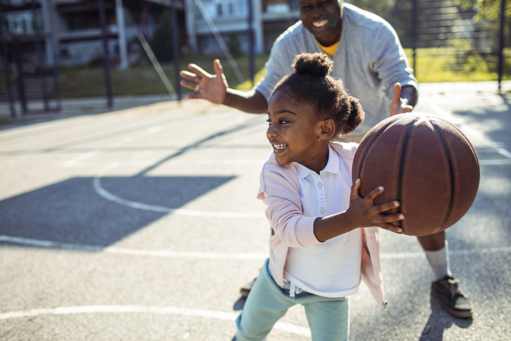 Young girl playing basketball with her father