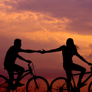 Two people reaching out to each on while riding bikes