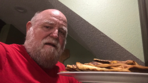 A selfie of a man with a white beard and red t-shirt stands in his kitchen with low-carb tortillas.