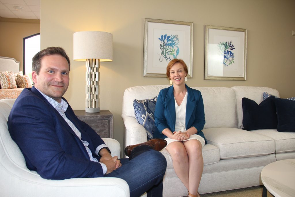 Amy McGeady, new CEO, and Baker Harrell, founder, sit in a light and white living room. Both are smiling and looking at the camera. 