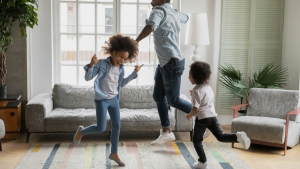 A black man with two young, black children dancing and laughing inside a home