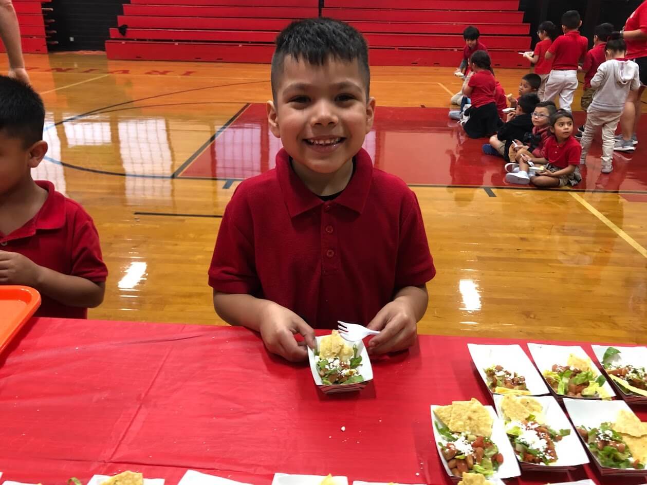 An elementary student smiling with a healthy meal