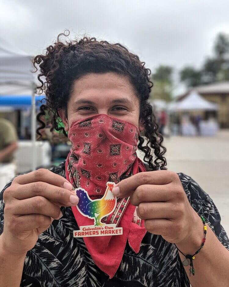 A woman holding a Galveston's Own Farmers Market sticker