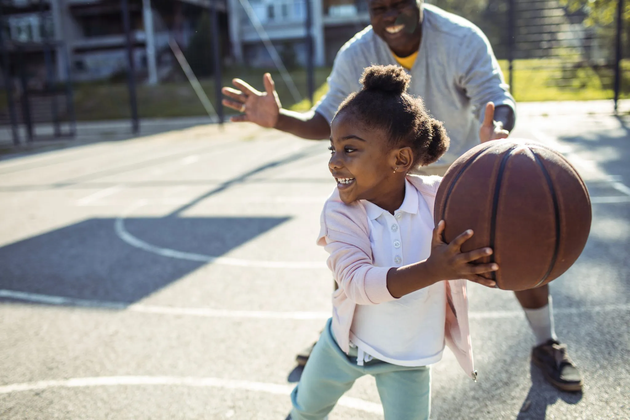 A young girl playing basketball with her father